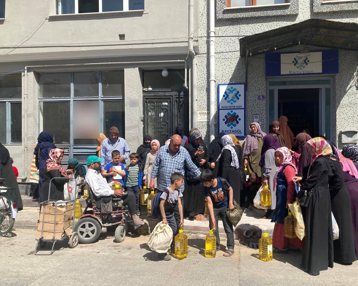 Dağıtım gününde yağ ve gıda paketlerini teslim alan aileler